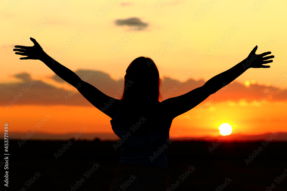 Woman silhouette celebrating stretching arms at sunset