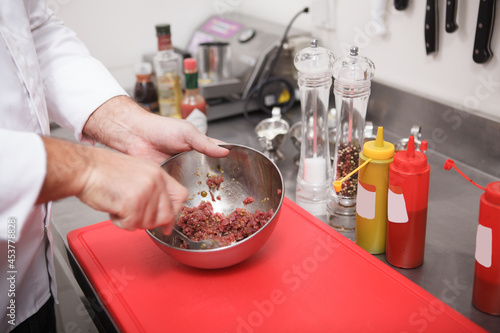 Close up of chefs hands stirring chopped beef for tartar in a metal bowl
