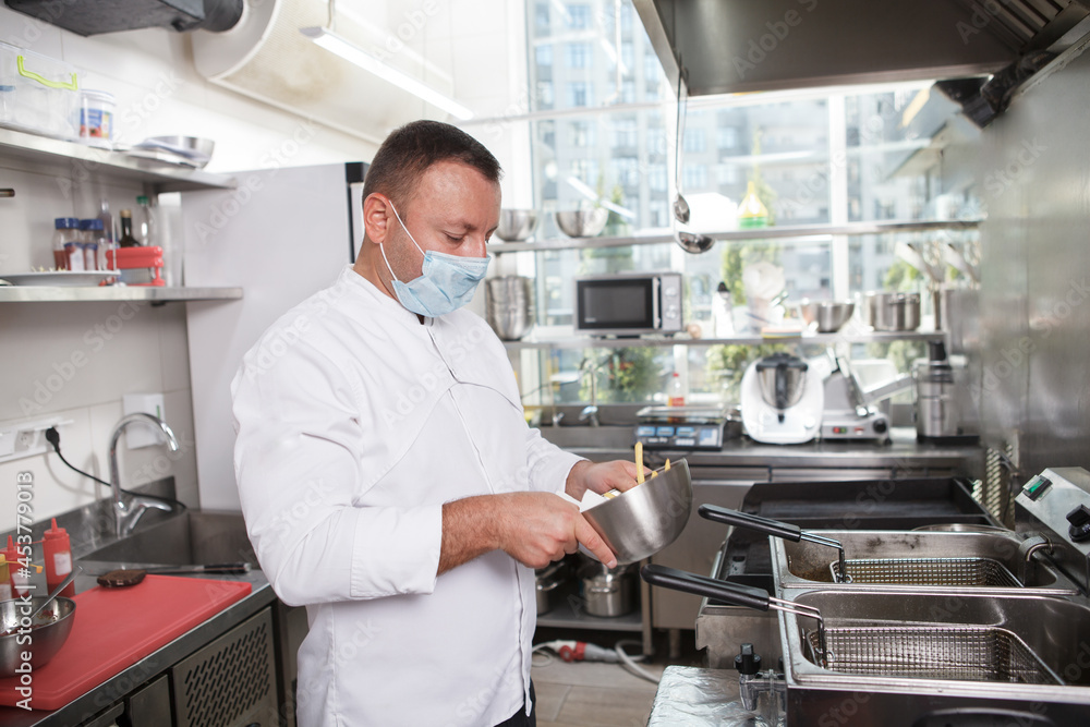 Male chef wearing medical face mask while working at restaurant kitchen, copy space Male chef wearing medical face mask while working at restaurant kitchen, copy space