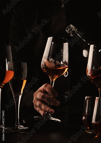 Sommelier pouring rose wine into glass at wine tasting in winery, bar or restaurant. Black toned image photo