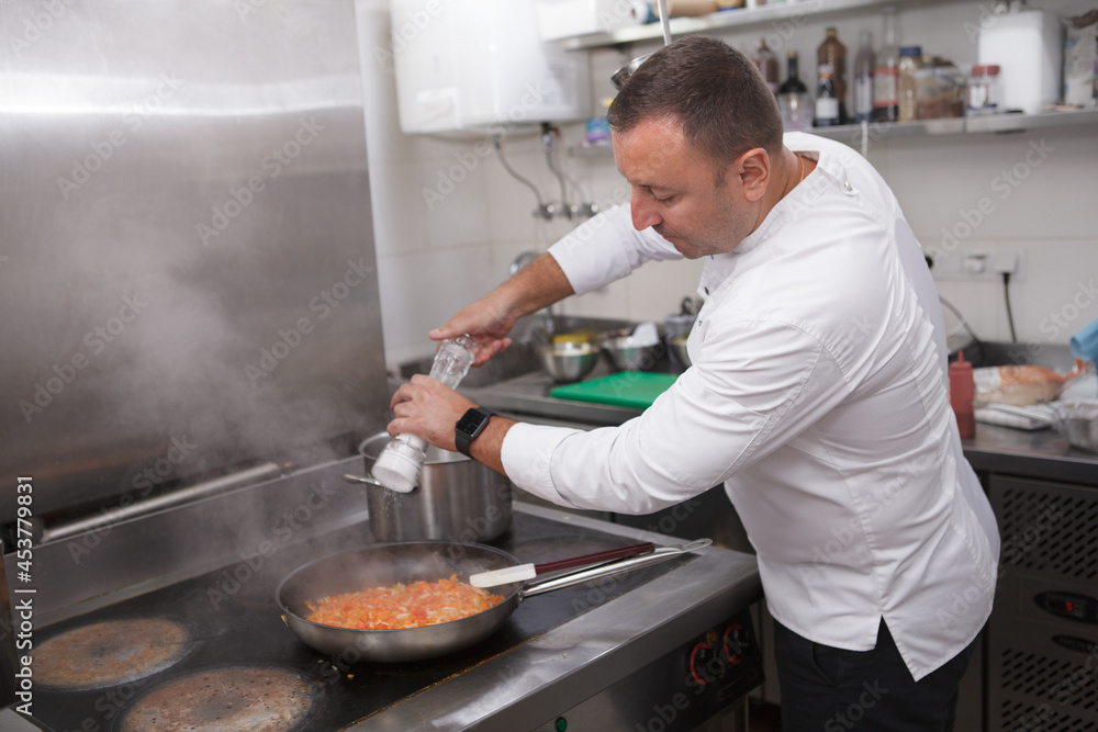 Chef salting frying vegetables in the pan, copy space Chef salting frying vegetables in the pan, copy space