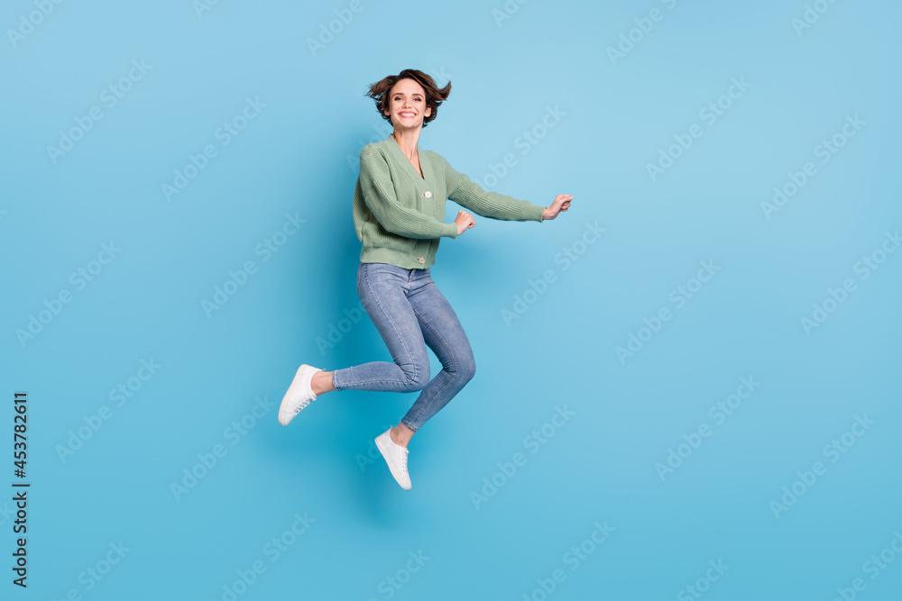 Full length photo of sweet cute young lady wear green cardigan jumping high isolated blue color background