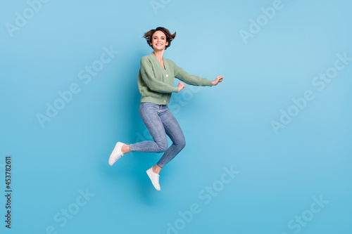 Full length photo of sweet cute young lady wear green cardigan jumping high isolated blue color background