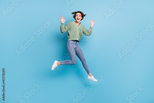 Full length photo of impressed funny young lady wear green cardigan jumping high isolated blue color background © deagreez