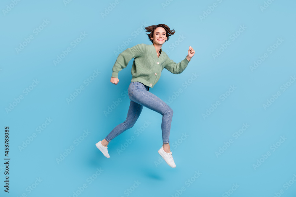 Full length photo of sweet charming young girl dressed green cardigan jumping high running fast isolated blue color background