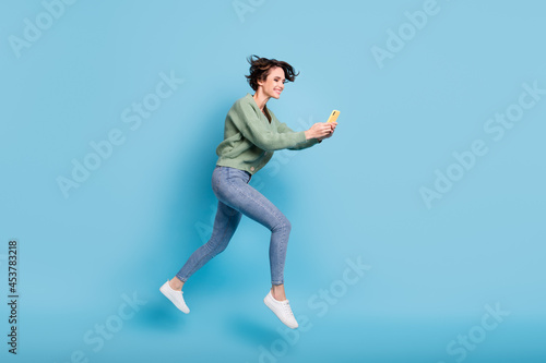Photo of pretty hurry young woman wear green cardigan jumping running holding modern device isolated blue color background