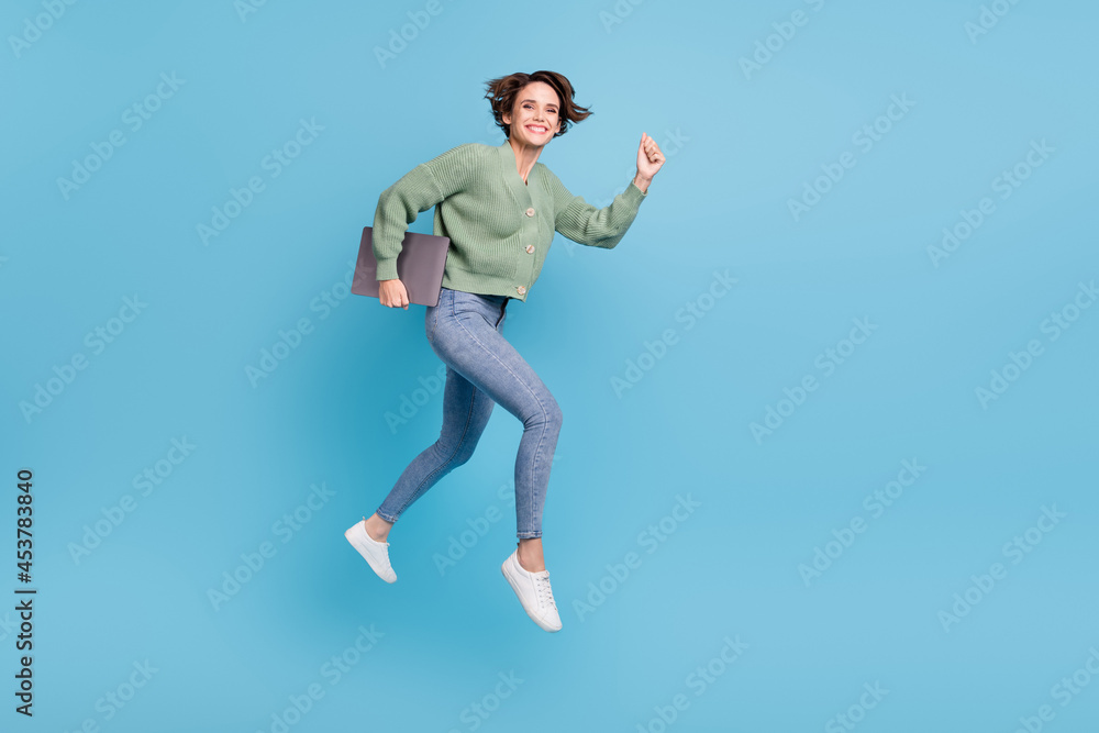 Full length photo of excited sweet young lady wear green cardigan jumping holding modern gadget isolated blue color background