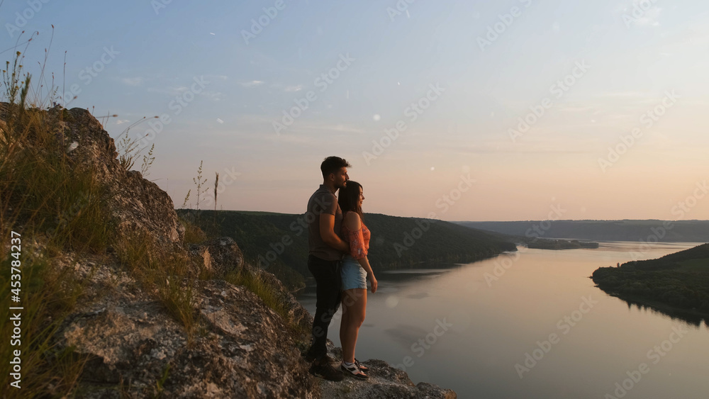 The romantic couple standing on rocky mountain top above the river