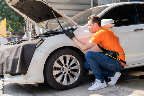 Male mechanic working at the garage. Male car mechanic examining, repair and maintenance under hood of car at auto car repair service. Car service and Maintenance concept