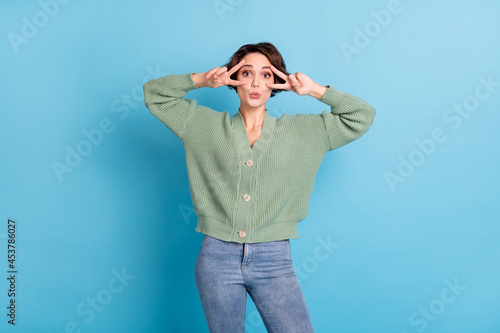 Portrait of pretty positive person two arms fingers show v-sign near eyes isolated on blue color background