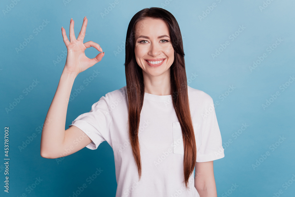 Fototapeta premium Portrait of woman gesturing ok sign fingers isolated on blue background