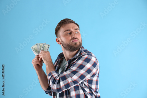 Greedy young man hiding money on light blue background photo