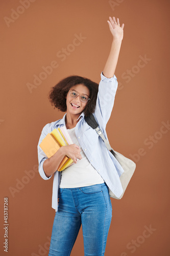 Portrait of excited teenage girl with students book waving with hand