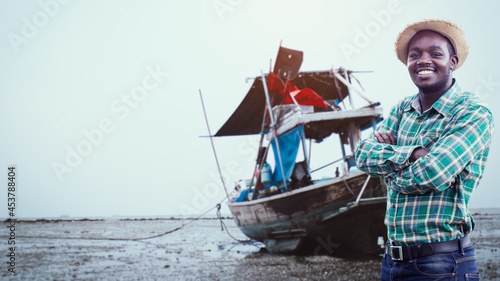Photos A smiling African fisher man stands beside his fishing boat