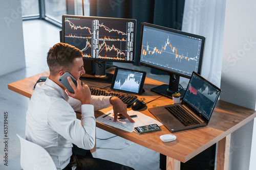 Stock market. Young businessman in formal clothes is in office with multiple screens
