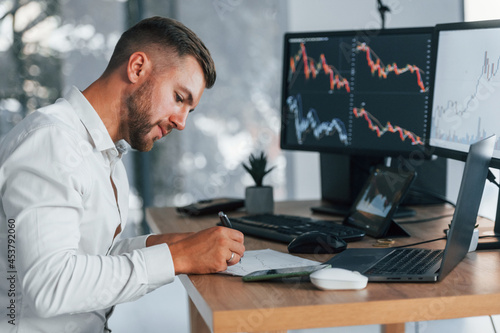 Young businessman in formal clothes is in office with multiple screens