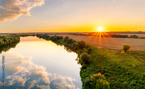 Scenic view at beautiful summer river sunset with reflection on water with green bushes, grass, golden sun rays, calm water ,deep cloudy sky and glow on a background, spring , evening landscape