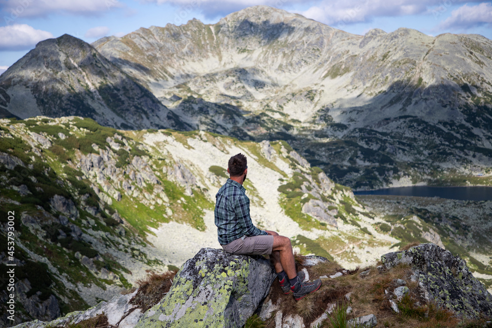 handsome man sitting on mountain top in amazing summer landscape handsome man sitting on mountain top in amazing summer landscape