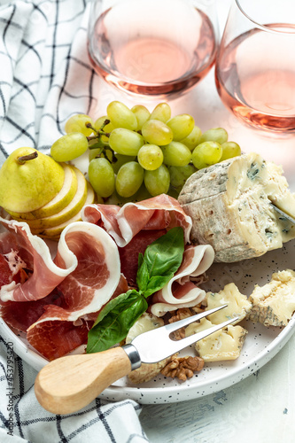 piece of blue cheese nuts and honey, prosciutto with vibrant grapes, rose wine, cheese knife, forks, nuts and honey, party celebration concept. top view
