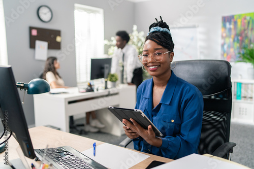 Working in office corporate duties elegant beautiful ambitious businesswoman sitting at desk with tablet making report writing back messages emptying email inbox corporate life, co-workers talking