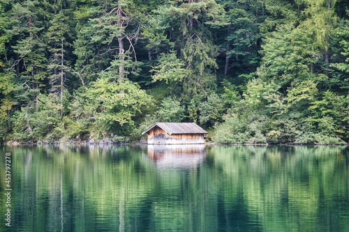 Beautiful green lake with a boats house in the forest and mountains