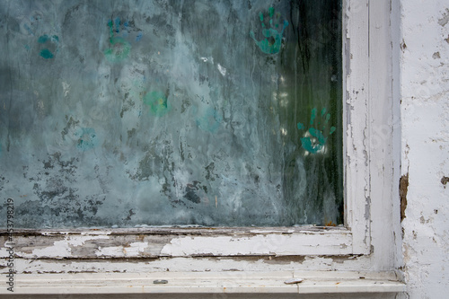 Schmutzige Scheibe in einem verwitterten Fensterrahmen mit bunten handabdrücken aus Fingerfarbe, verlassener Kindergarten, Schule ect
