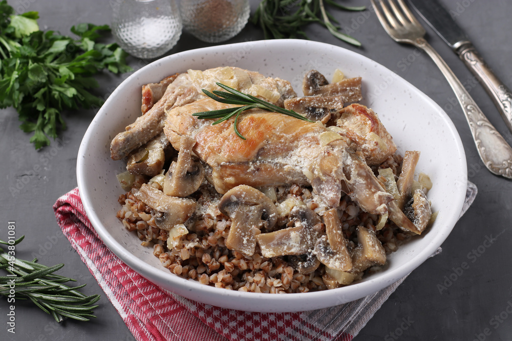 Rabbit meat with buckwheat, mushrooms and sour cream sauce in a light plate on a dark background Rabbit meat with buckwheat, mushrooms and sour cream sauce in a light plate on a dark background