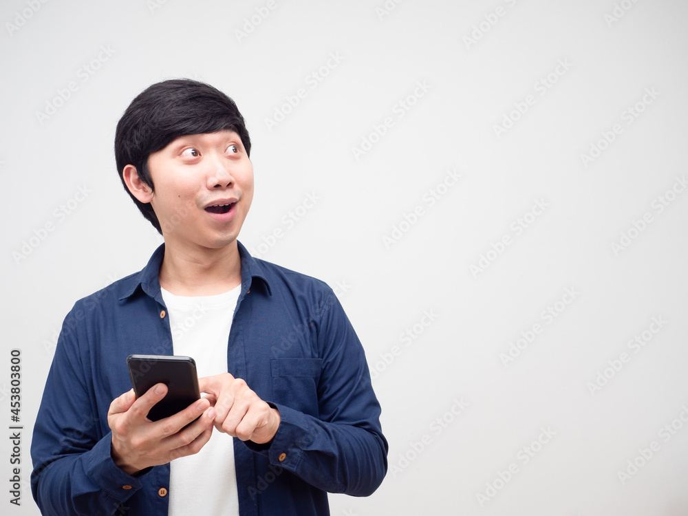 Asian young man holding and press mobile phone in his hand feeling excited and lookign at copy space white isolated Asian young man holding and press mobile phone in his hand feeling excited and lookign at copy space white isolated