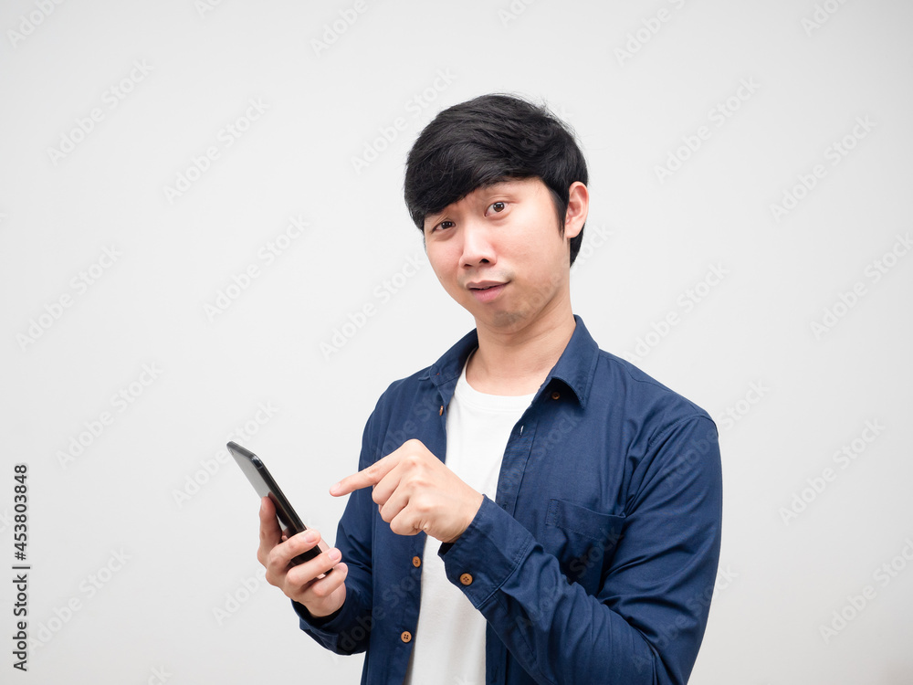 Young man point finger at mobile phone in his hand feeling confused white background Young man point finger at mobile phone in his hand feeling confused white background