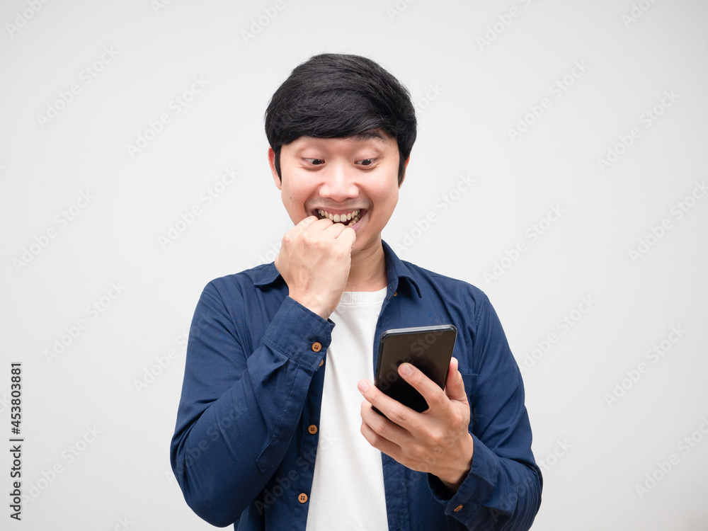 Young asian man looking at mobile phone in his hand feeling excited Young asian man looking at mobile phone in his hand feeling excited