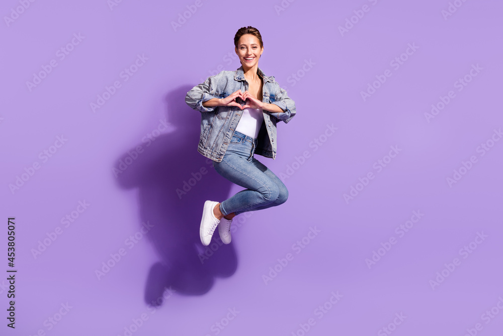 Full body photo of young happy cheerful woman jump up make fingers heart shape isolated on violet color background