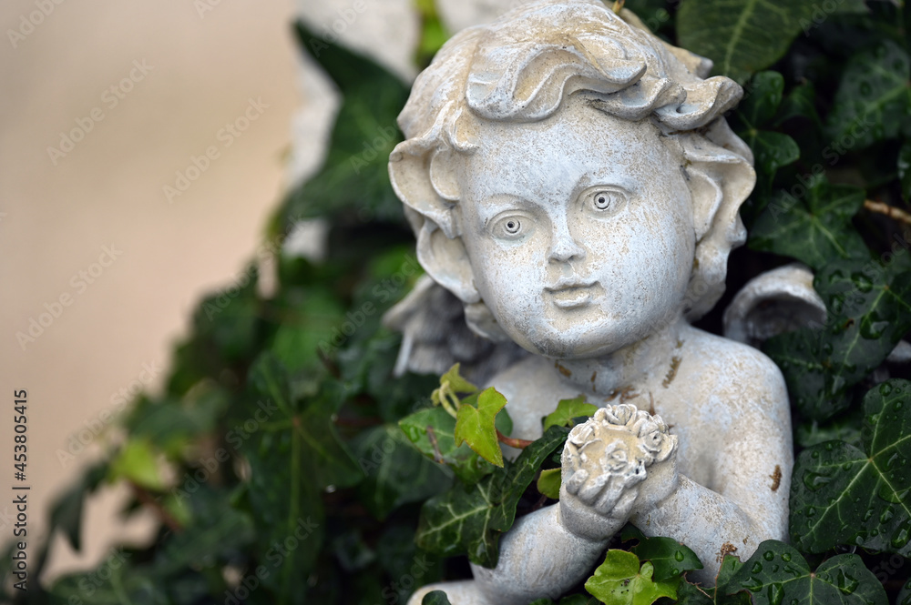 An old, weathered sandstone sculpture of a praying angel who is partially covered with ivy. 
