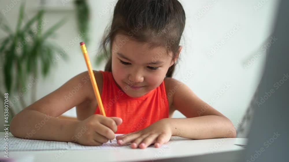Online home school for junior schoolchildren. Spbd Little Asian girl student writes in notebook during distance lesson via computer at home closeup Online home school for junior schoolchildren. Spbd Little Asian girl student writes in notebook during distance lesson via computer at home closeup