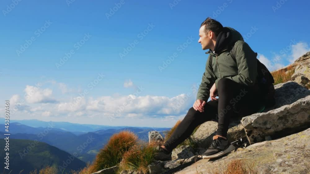 Young guy traveler enjoys the view of the mountain range while sitting on the top of the cliff. Young guy traveler enjoys the view of the mountain range while sitting on the top of the cliff.