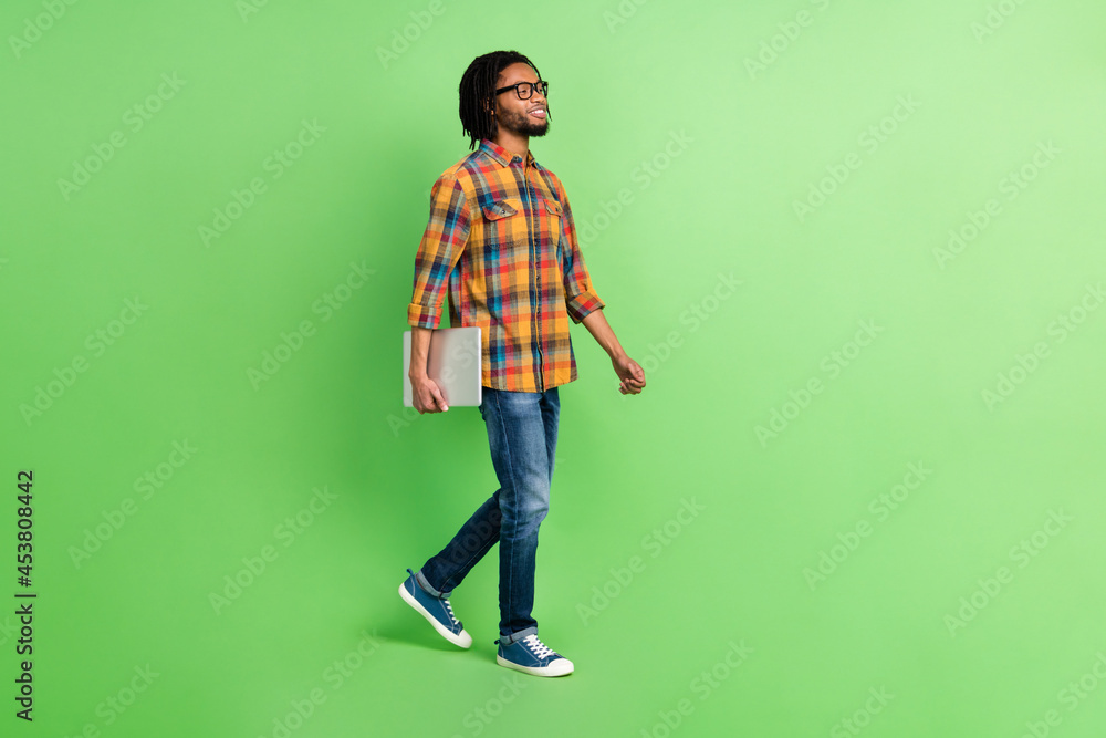 Photo of sweet confident dark skin guy dressed shirt glasses walking holding modern device empty space isolated green color background Photo of sweet confident dark skin guy dressed shirt glasses walking holding modern device empty space isolated green color background