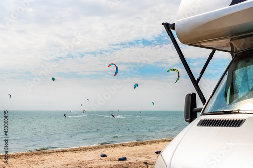 Panoramic view of many surf board kite riders on sand beach watersport spot on bright sunny day against rv camper van vehicle at sea ocean coast at surfing camp. Fun adventure travel sport acitivity
