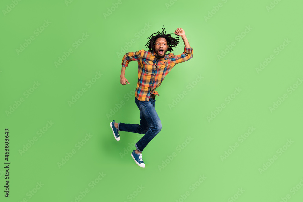 Photo of amazed african guy jump hurry run shout wear plaid shirt jeans isolated green color background