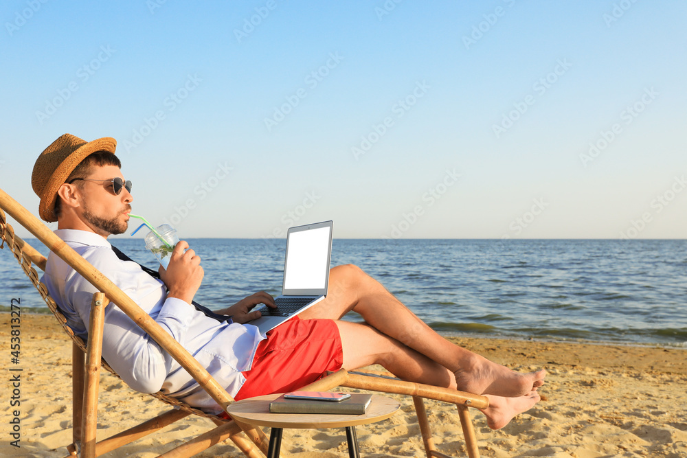 Man with laptop and drink resting on beach. Business trip