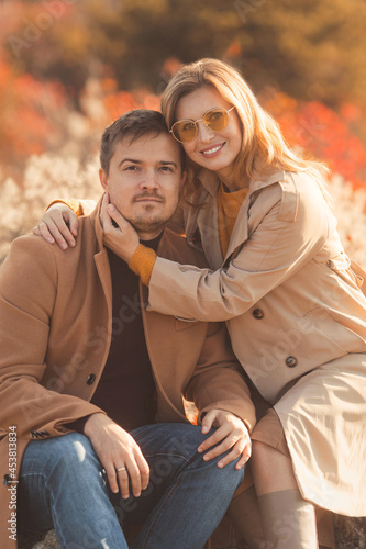 Happy family hugging on a walk in the fall park. Portrait of a caucasian woman and man in beautiful fashion outfits on a sunny autumn day in forest. Family lifestyle concept.