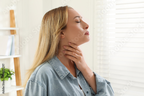 Young woman doing thyroid self examination near window at home photo