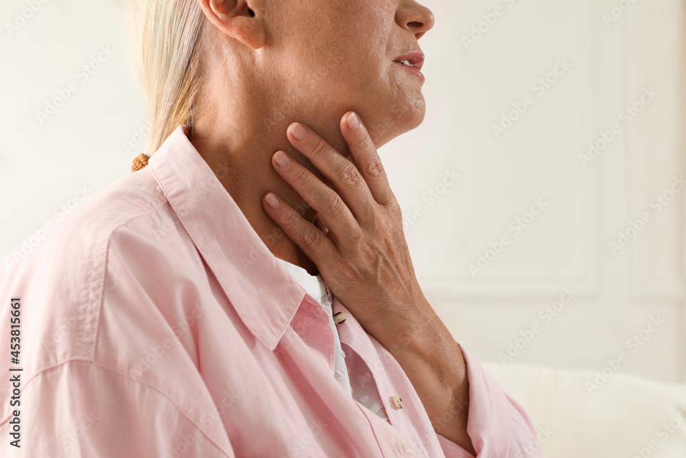 Mature woman doing thyroid self examination on light background, closeup Mature woman doing thyroid self examination on light background, closeup