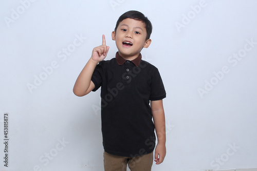 The Asian boy who was wearing a black t-shirt was looking ahead with his index finger raised with an expression as if he had an idea. White background. 