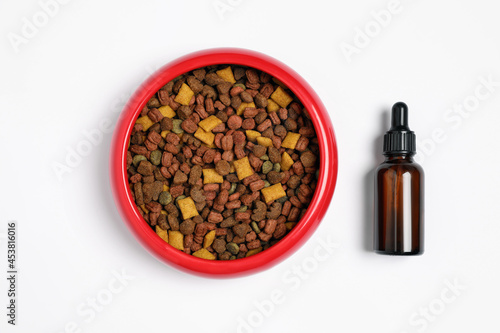 Glass bottle of tincture near dry pet food in bowl on white background, top view
