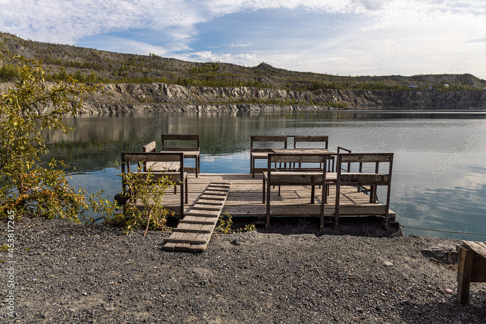 Pontoon with a wooden table and benches for relaxation is on the blue water of the lake