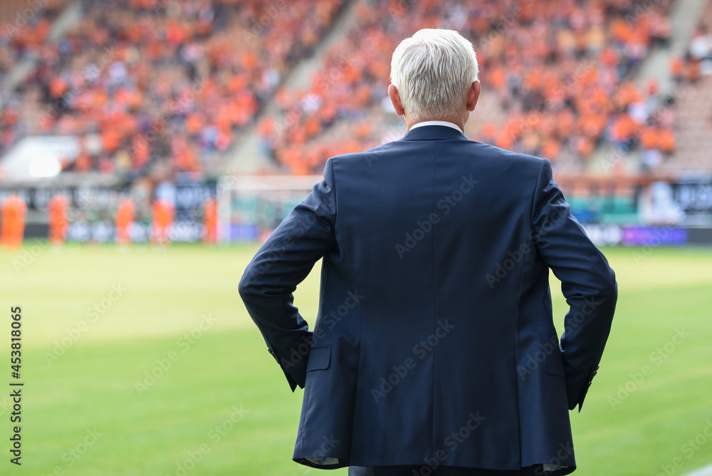 Head coach's back and soccer match at the stadium in the background