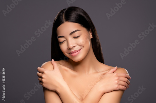 Photo of cute lovely positive chinese lady hands hug shoulders close eyes enjoy soft skin isolated grey color background