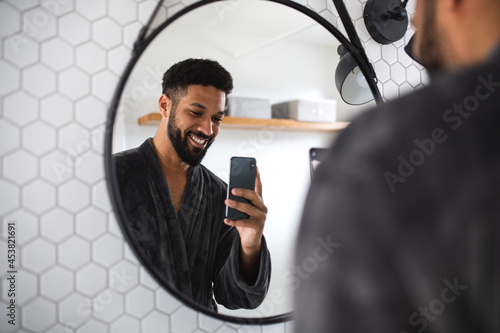 Young man with bathrobe indoors in bathroom at home, taking selfie. photo