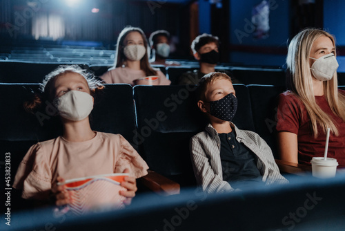Mother with happy small children watching film in the cinema  coronavirus concept.