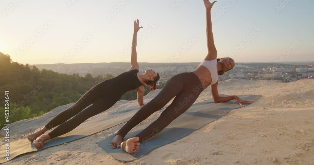 Full length view of the two young flexible women doing sport yoga exercise asana in beautiful mountains landscape on the sunrise Full length view of the two young flexible women doing sport yoga exercise asana in beautiful mountains landscape on the sunrise