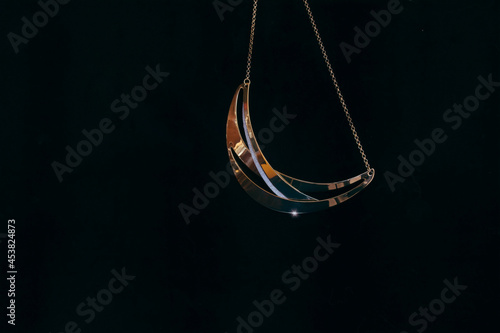 A gold and diamond necklace in the shape of a crescent moon hanging from gold chain, black background, nobody photo